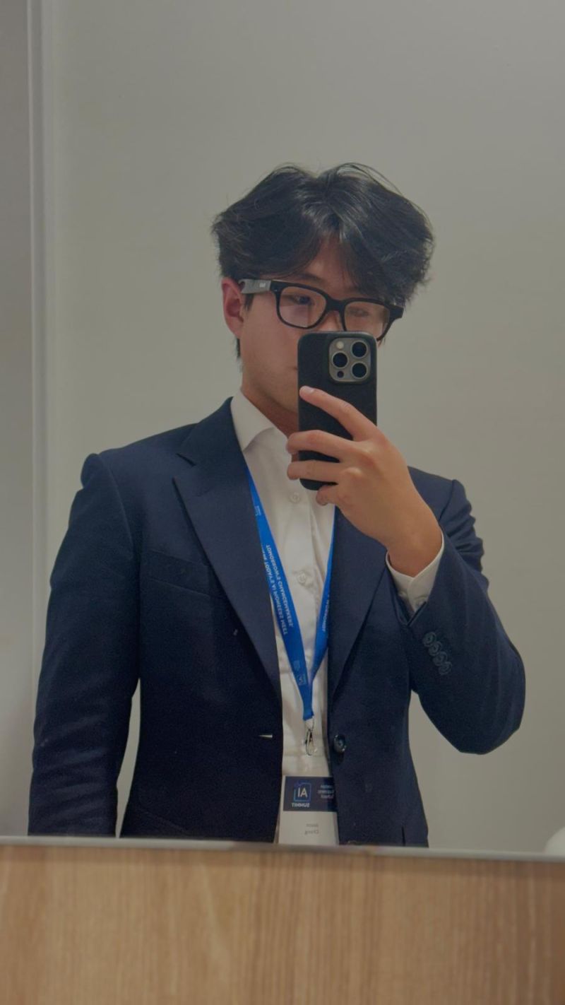 A mirror portrait in a navy suit with an AI Summit lanyard.